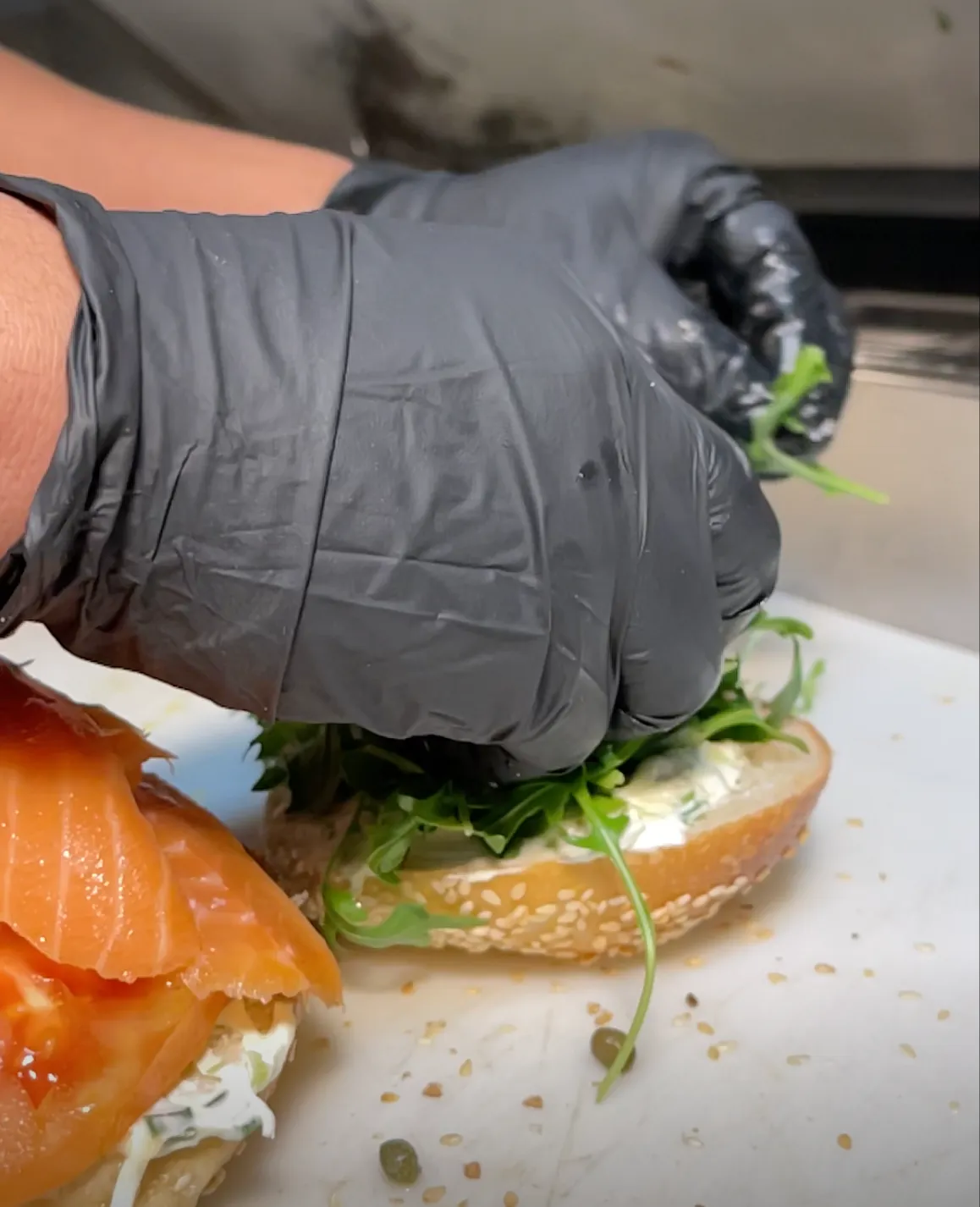 Fresh arugula being placed on a bagel