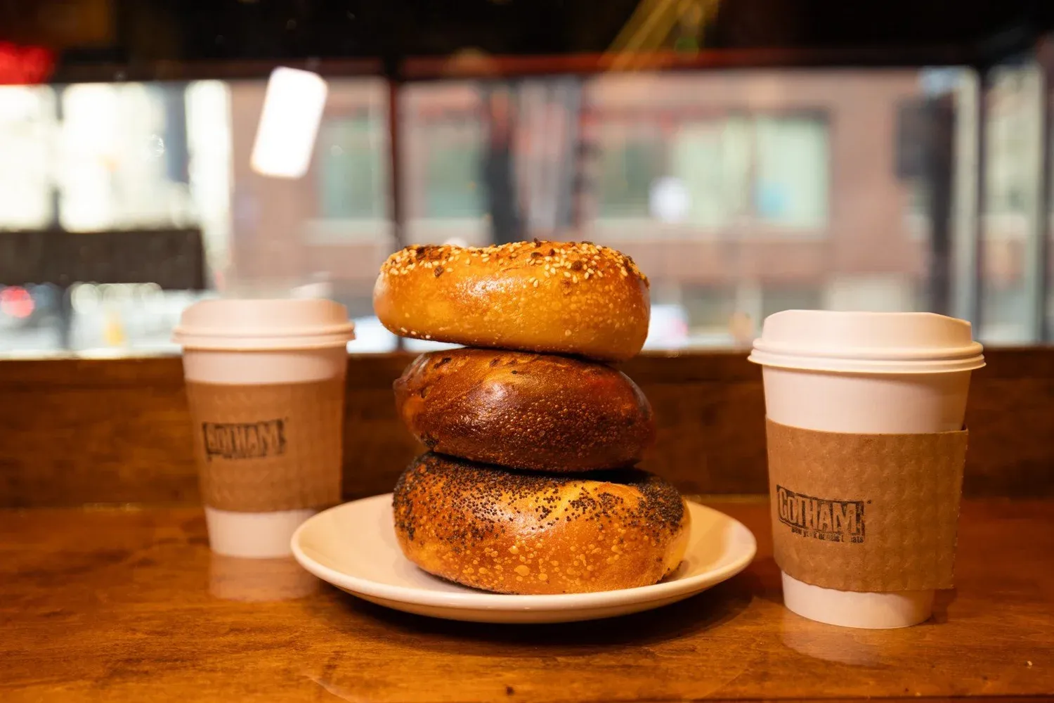 Three bagels on a plate with two coffees on a table