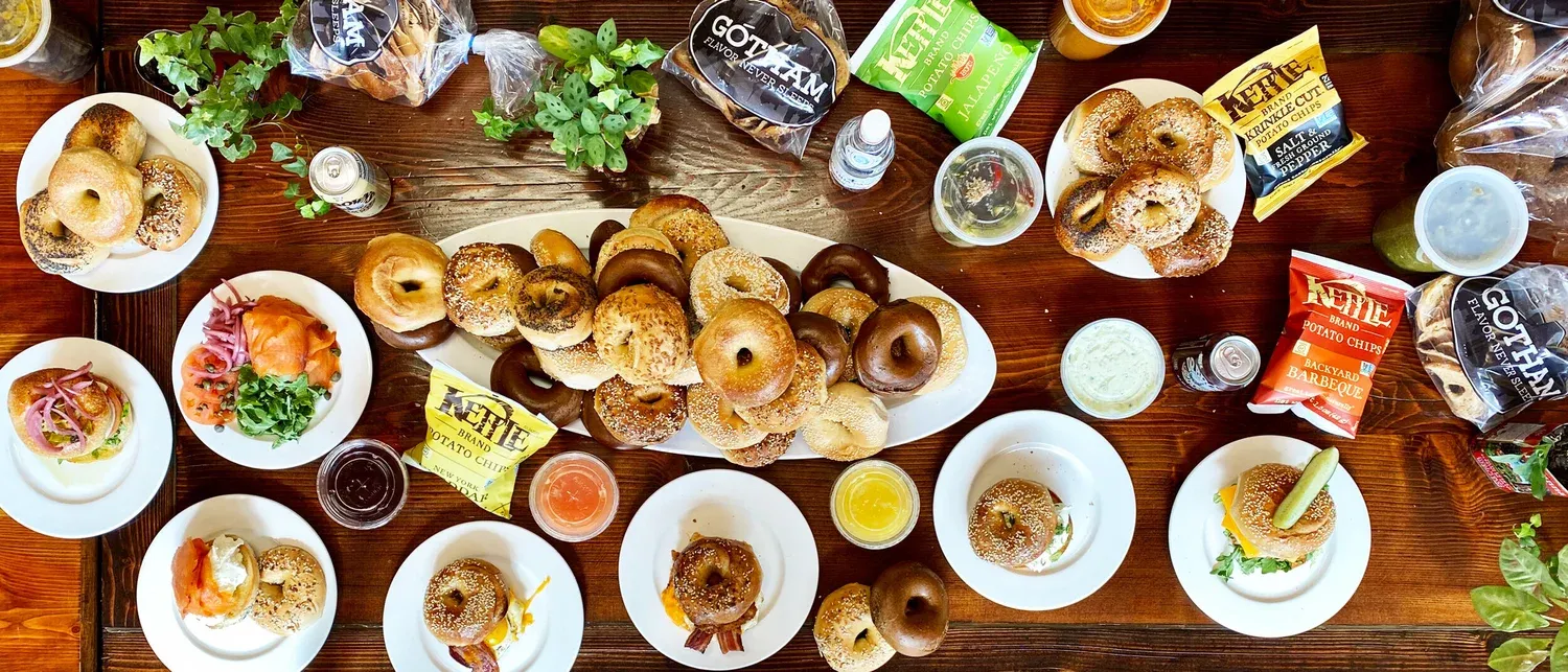 A catering table set with platters of assorted Gotham bagels, bagel sandwiches, spreads and chips