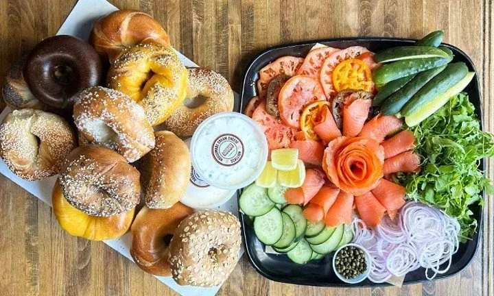 Gotham Bagels catering: a dozen assorted hand-rolled bagels beside a lox platter with tomato, cucumber, arugula, red onion, capers and cream cheese