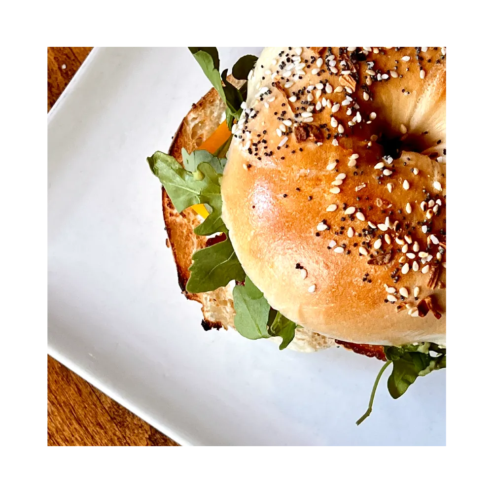 Everything bagel sandwich with arugula on a white plate